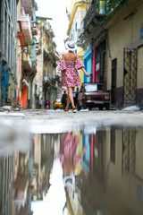 Fototapeta na wymiar Woman in a bright dress and white hat walks on a city street of Cuba