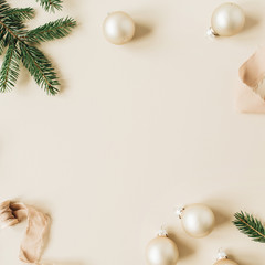 Christmas / New Year holiday composition. Mock up frame with blank copy space made of fir needle branches, ribbon and Christmas baubles on beige background. Flat lay, top view festive concept.