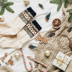 Fototapeta na wymiar Christmas / New Year composition. Woolen socks, gift box, fir branches, Christmas baubles, ginger cookies, stick candies, knitted plaid, decorations. Flat lay, top view decorated holiday background.