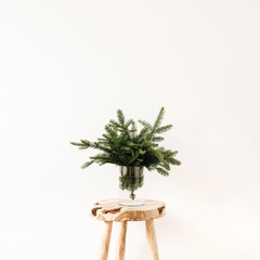 Bouquet of fir-tree branches on solid wooden stool on white background. Minimal Christmas, New Year...