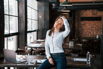 Fototapeta premium Sitting and touching the hair. Businesswoman in official clothes is indoors in cafe at daytime