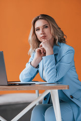 She listens to you carefully. Businesswoman with curly blonde hair indoors in room with orange colored wall and wooden table