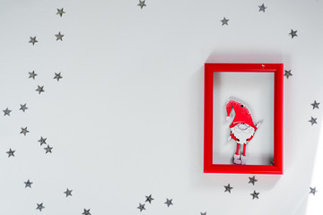 Funny handmade red gnom on frame with silver stars on white christmas background for a greeting card. Copy space flat lay