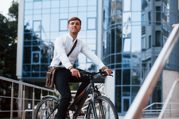 Thinks about future. Businessman in formal clothes with black bicycle is in the city