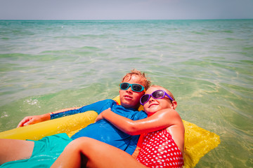happy kids, boy and girl, swim on floatie on beach vacation
