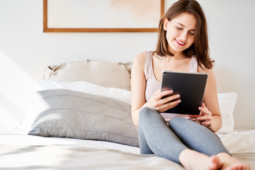 Photo of woman with tablet in hands sitting on bed .