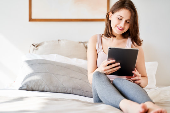 Photo of woman with tablet in hands sitting on bed .