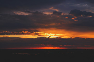 Special sunset over the river and forest. The warm colors of the sun. Bright blue unusual sky. Black silhouette of the forest.