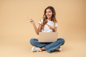 Image of cheerful woman sitting on floor with silver laptop