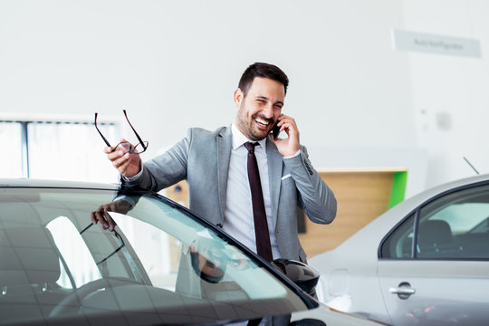 Businessman Talking On Phone Near Car In Modern Dealership.