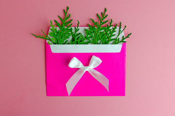 New Year's composition. A pink envelope with fir branches in it and a white bow on a pink background. Background about christmas. Save the space, flat lay.