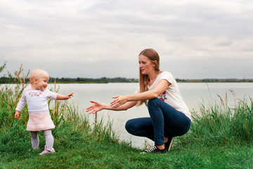 Fototapeta premium A girl learns to walk with her mother in nature. Mom and daughter, learning and development. The first steps of the child. Happy moments of life.