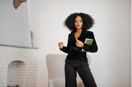 Stylish african american woman in black posed at room against fire place read books.