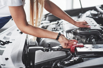 Under the hood. Car addicted woman repairs black car indoors in garage at daytime