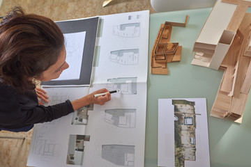  Young woman works as an architect in an office. She is brunette and Latina has a black shirt and different jobs on her table.