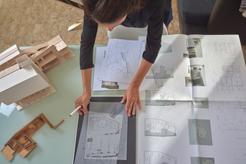  Young woman works as an architect in an office. She is brunette and Latina has a black shirt and different jobs on her table.