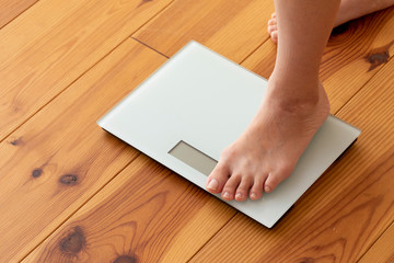 木目の床と体重計に乗る若い女性の足元