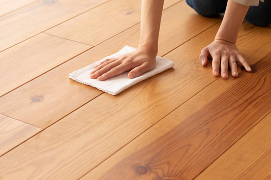 木目の床を雑巾で拭く若い女性の手元