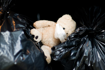 a teddy bear in a medical mask lies in the trunk of a car on garbage bags