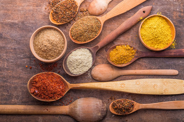 Heaps of various ground spices in wooden spoons on wooden background. Georgian spices, Indian spices, Arabian spices. Spice variety. Herbs and spices