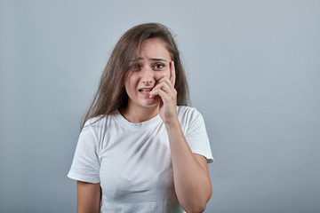 Woman with long hair over isolated grey wall nervous and scared. Dressed in a white t shirt Sticks her fingers in her mouth and experiences a shocking moment