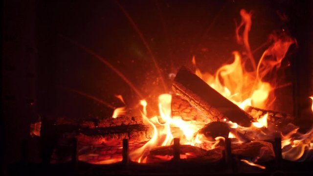 Slow motion video of burning fire and flying sparkles in the firepalce at night