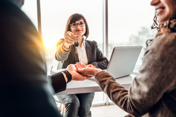 Cropped image of happy family couple making purchase their first house, taking key from female...