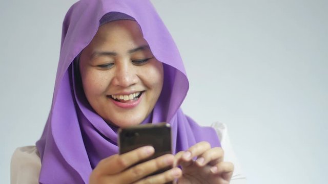 Beautiful Asian muslim woman smiling happily while doing chat reading message on her smart phone