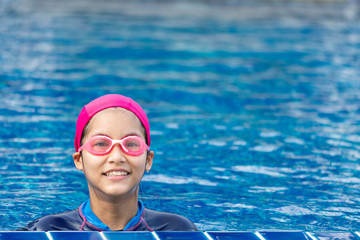 Girls wearing swimsuits cap and swimming goggles. On the edge of the pool.