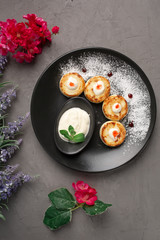 pancakes with sour cream in a black plate decorated with icing sugar