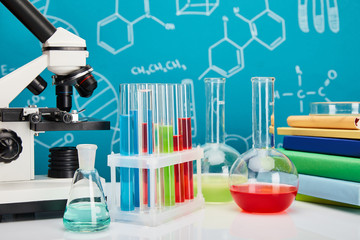 microscope, books, glass test tubes and flasks with colorful liquid on blue background with...
