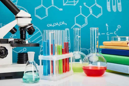 microscope, books, glass test tubes and flasks with colorful liquid on blue background with molecular structure