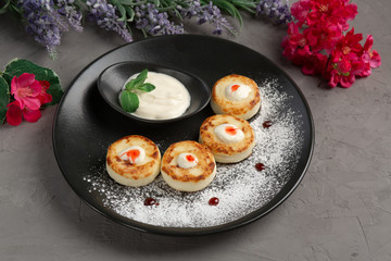 pancakes with sour cream in a black plate decorated with icing sugar