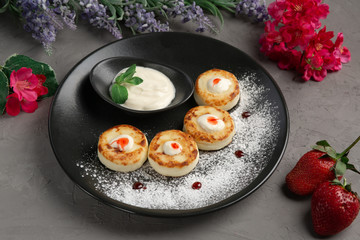 pancakes with sour cream in a black plate decorated with icing sugar