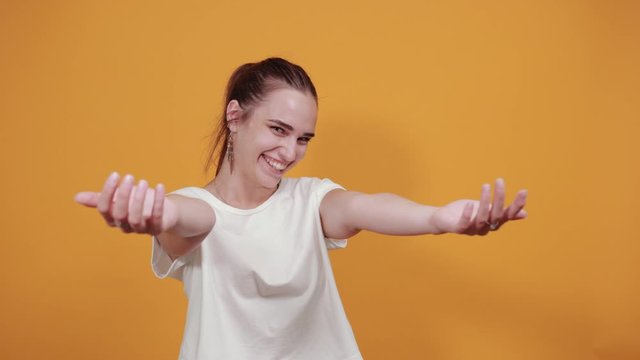 Gorgeous girl opening her arms wide to give a warm welcome to someone. She is wearing white t shirt and smiling brightly to give a decent gesture.