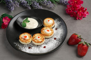 pancakes with sour cream in a black plate decorated with icing sugar