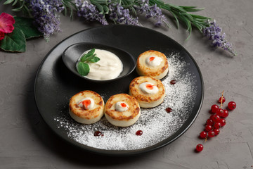 pancakes with sour cream in a black plate decorated with icing sugar