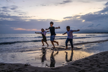 Three kids running on the beach at sunset