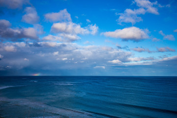 Fototapeta na wymiar Regenbogen hinter den Wolken über dem Meer