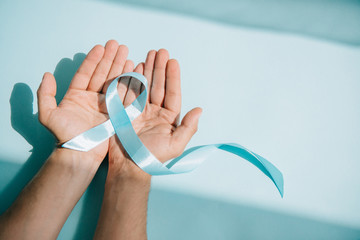 cropped view of male hands with blue awareness ribbon on white background