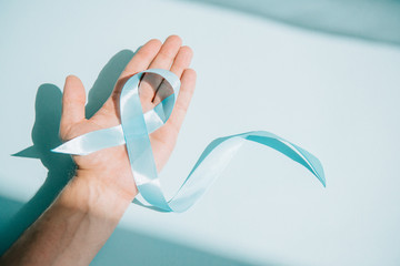 partial view of male hand with blue awareness ribbon on white background