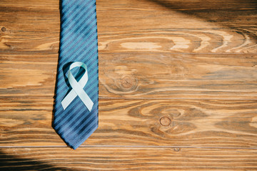 tie and blue awareness ribbon on wooden surface