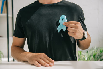 partial view of man in black t-shirt holding blue awareness ribbon