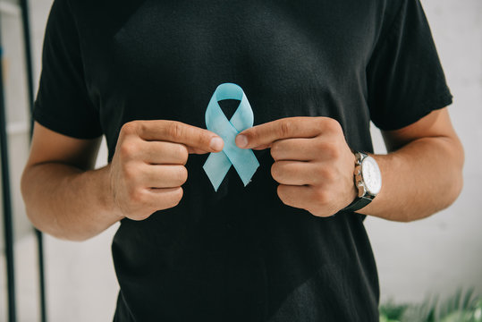 cropped view of man in black t-shirt holding blue awareness ribbon