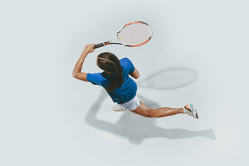 Young woman in blue shirt playing tennis. She hits the ball with a racket. Indoor studio shot...
