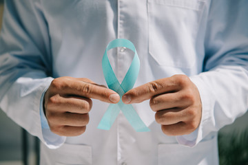 partial view of doctor in white coat holding blue awareness ribbon