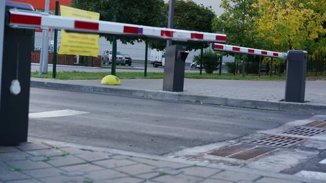 timelapse red and white barrier passes various cars to and from parking lot against green and golden autumn city park