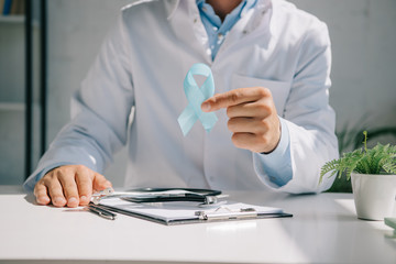 cropped view of doctor sitting at desk and showing blue awareness ribbon