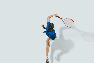 Young woman in blue shirt playing tennis. She hits the ball with a racket. Indoor studio shot isolated on white. Youth, flexibility, power and energy. Negative space. Top view. - obrazy, fototapety, plakaty