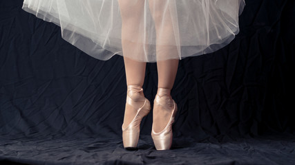 Close-up of dancing legs of ballerina wearing white pointe on a black background.